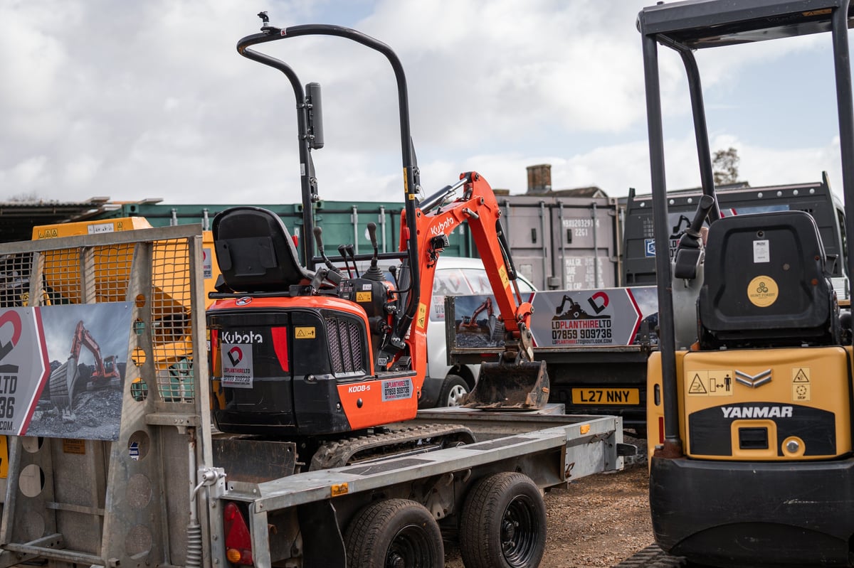 Orange mini excavator on a flatbed trailer with a yellow Yanmar excavator beside it
