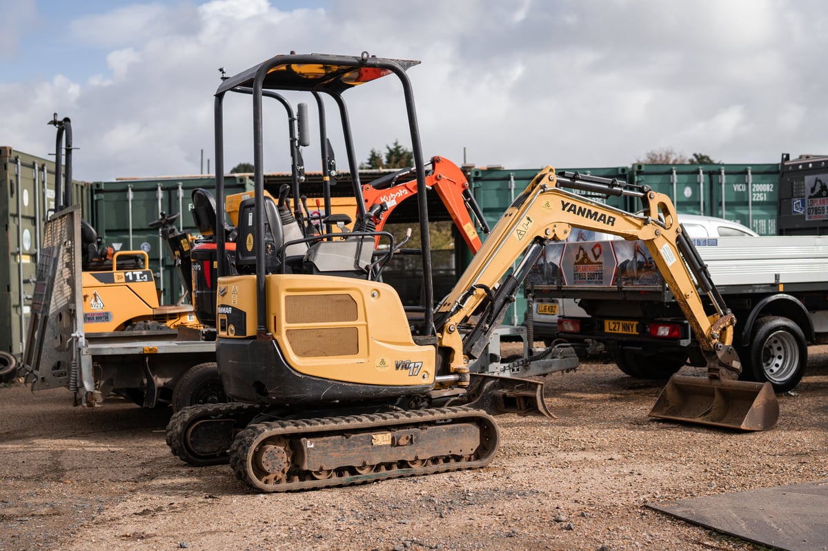 Yellow compact excavator parked at a construction site with other machinery behind